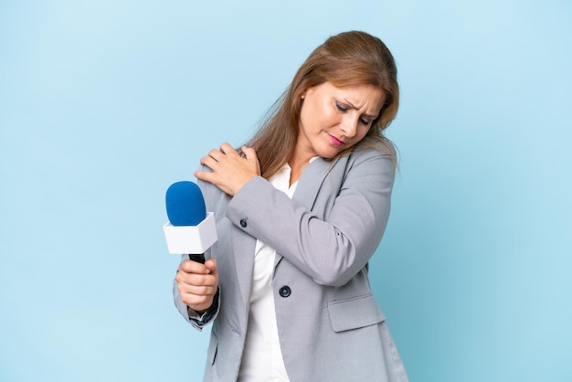 Prezenterka telewizyjna w średnim wieku na odizolowanym niebieskim tle cierpiąca na ból barku za wysiłek