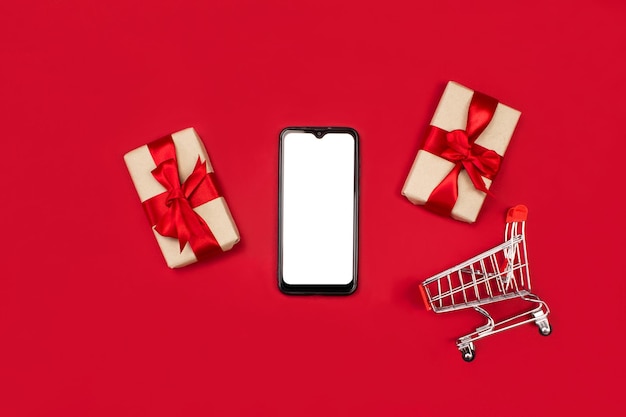 Prezenty smartphone makieta wózek na zakupy płasko leżał na czerwonym tle miejsca kopiowania Świąteczne zakupy