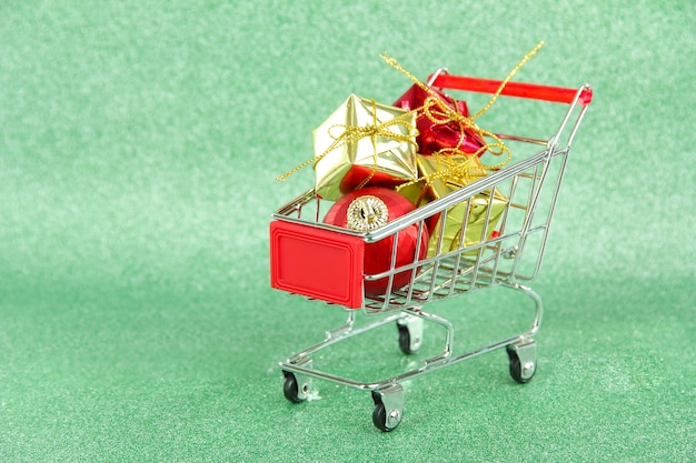 Prezenty świąteczne w wózku na zakupy, na zielonym błyszczącym tle