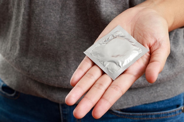 Prezerwatywy gotowe do użycia w ręce młodego mężczyzny, dają kondom bezpiecznego seksu na łóżku. Światowy dzień AIDS
