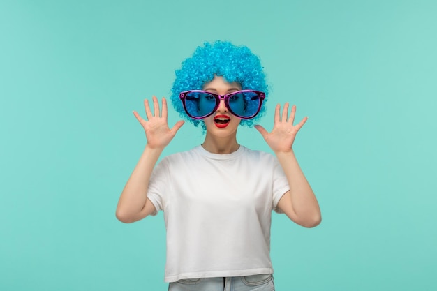 Prima Aprilis zaskoczona klaun dziewczyna z dłońmi w górę duże różowe niebieskie okulary zabawny kostium niebieskie włosy