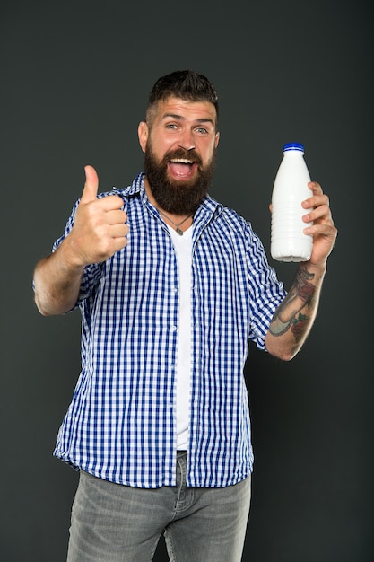 Probiotyki jogurtowe i prebiotyki. Brodaty mężczyzna trzyma białą butelkę z mlekiem. Brutalny kaukaski hipster pije mleko. Dieta laktozowa. Opieka zdrowotna i dieta. Produkty mleczne. Spożywanie laktozy. Zdrowe odżywianie.