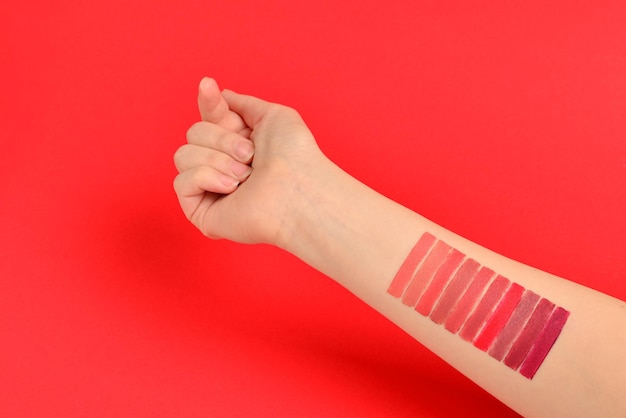 Próbki szminki na rękę kobiety na białym tle na czerwonym tle.