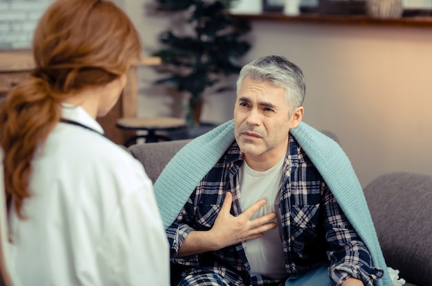 Zdjęcie problemy ze zdrowiem. smutny, ponury mężczyzna patrzący na lekarza, mówiący o objawach swojej choroby