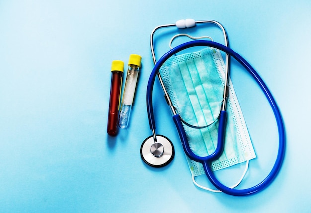 Probówka z próbką krwi Test koronawirusa 2019-nCoV, stetoskop i maska lekarza na niebieskim tle. Koncepcja medyczna