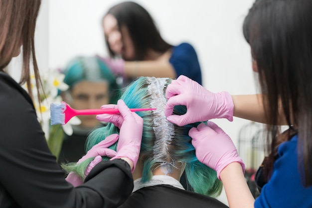 Proces farbowania włosów w gabinecie kosmetycznym dwóch fryzjerów nakłada farbę na włosy podczas rozjaśniania włosów