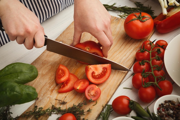 Proces gotowania gazpacho, tradycyjnej hiszpańskiej zimnej zupy ze świeżych warzyw. Ręka kobiety cięcie świeżych pomidorów, widok z góry