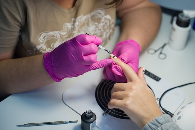 Proces kobiecego manicure w salonie kosmetycznym, żelowy lakier do paznokci.