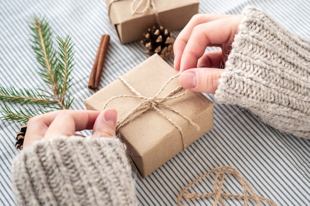 Zdjęcie proces pakowania stylowych, nowoczesnych prezentów na boże narodzenie i nowy rok. pudełka na prezenty wykonane z papieru kraft, sznurka i gałęzi choinki.