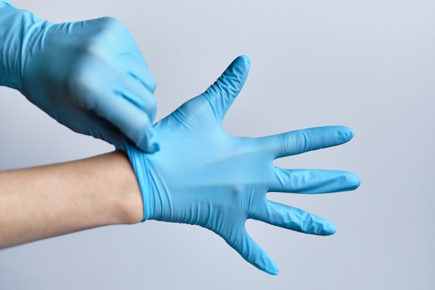 Proces zakładania niebieskich rękawiczek medycznych na ręce na białej przestrzeni.