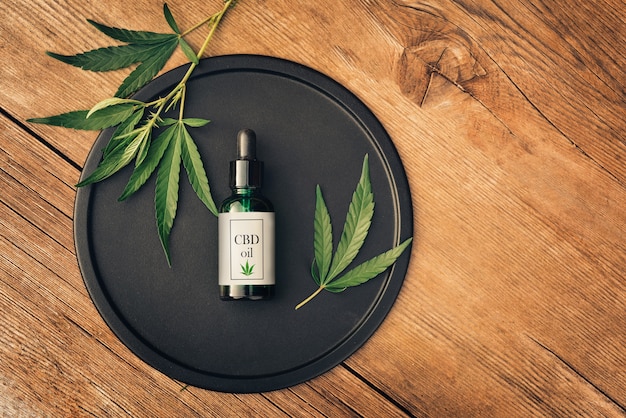 Produkt Medyczny Cannabs, Olej Cbd, Z Liśćmi Konopi Na Czarnym Naczyniu Na Drewnianym Stole. Leżał Na Płasko. Mockup Copy Spase