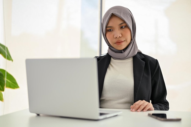 Profesjonalna azjatycka muzułmańska bizneswoman skupiająca się na swoim projekcie biznesowym za pomocą laptopa