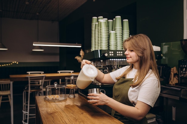 Profesjonalna baristka wlewająca mleko do kubka z gorącym napojem, robiąc cappuccino lub latte