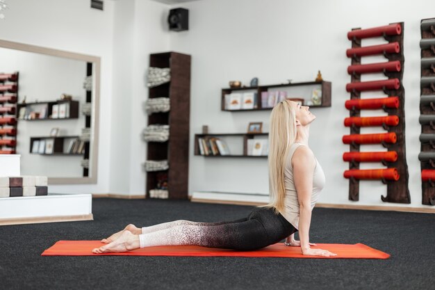 Profesjonalna młoda kobieta robi ćwiczenia na plecy w sali fitness na macie. Dziewczyna ćwiczy jogę, rozciąganie lub pilates.