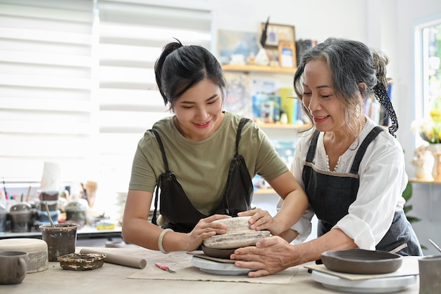 Profesjonalna nauczycielka w wieku szkolnym ucząca kobietę wykonywania miski ceramicznej z gliną w warsztacie