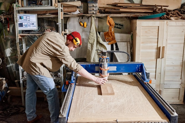 Profesjonalna stolarka dopasowująca frezarkę CNC do wykonywania drewnianych detali w warsztacie stolarskim