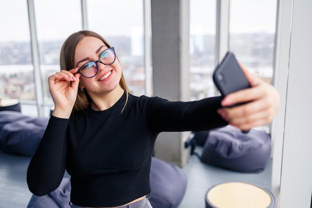 Profesjonalne Bizneswoman Dorosły Zajęty Sms-y Na Jej Telefon Komórkowy Na Sobie Koszulę I Spodnie Stojąc Przed Dużymi Szklanymi Oknami.