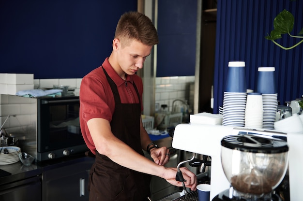 Profesjonalne parzenie kawy. Młody wyszkolony barista przygotowuje kawę na profesjonalnym ekspresie do kawy parowej.