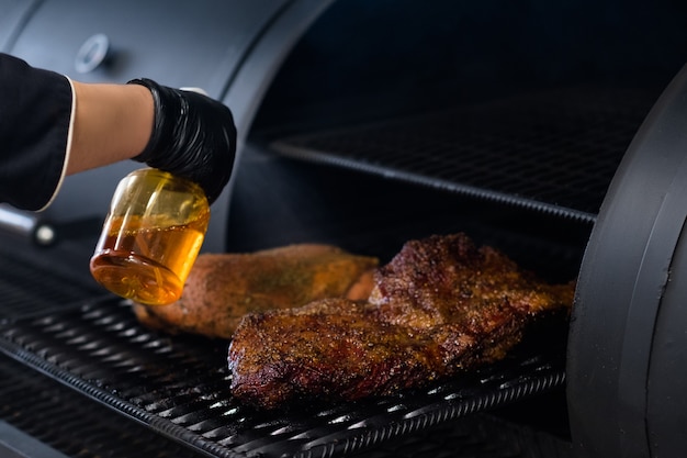 Profesjonalne urządzenie kuchenne. Szef kuchni rozpyla grillowane mięso w wędzarni BBQ.