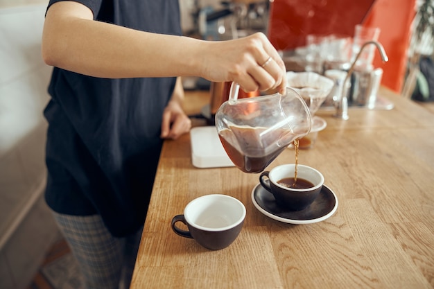 Profesjonalne zdjęcie baristy baristy przy ladzie w kawiarni nalewanie kawy filtrowanej w filiżance.