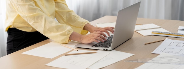 Profesjonalny architekt pracujący na laptopie w nowoczesnym biurze na stole roboczym ze sprzętem architektonicznym i planem rozproszonym wokół koncepcji życia i projektowania Skup się na dłoni Zbliżenie nakreślenia