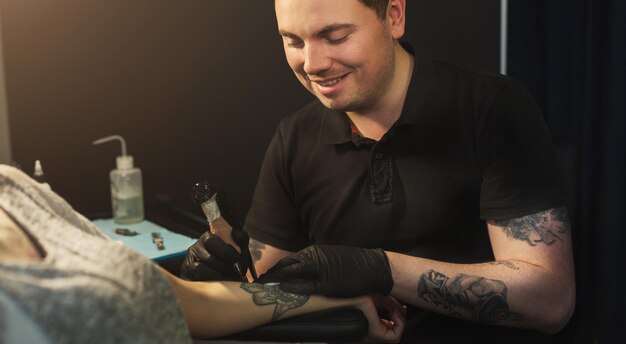 Profesjonalny Artysta Tatuator Robi Zdjęcie Na Rękę Kobiety Przez Maszynę. Tatuaz Sztuki Na Ciele. Sprzęt Do Robienia Czarnego Tuszu Ze Sztuki Jartattoo.