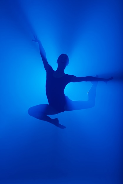 Zdjęcie profesjonalny balerina taniec balet w dymie. kobieta w czarnym body na tle reflektorów.