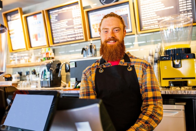 Profesjonalny barista młody rudowłosy imbir brodaty mężczyzna w czarnym fartuchu pracujący w kawiarni