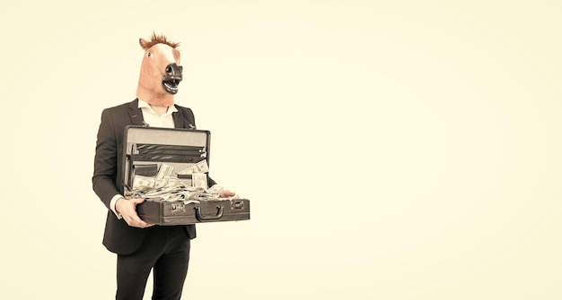 Profesjonalny biznesmen nosi maskę głowy konia w formalnej odzieży, trzymając walizkę z banknotami dolarowymi na białym tle, kopia przestrzeń pieniądze