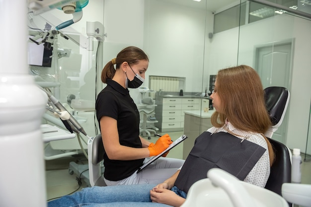 Profesjonalny dentysta ze schowkiem rozmawia lub nagrywa diagnozę pacjenta przed lub po zabiegu