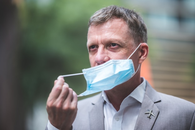 Profesjonalny dorosły biznesmen noszący chirurgiczną maskę na twarz w celu ochrony przed koronawirusem COVID-19