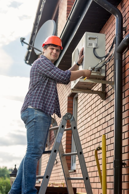 Profesjonalny elektryk naprawiający klimatyzator na zewnętrznej ścianie budynku