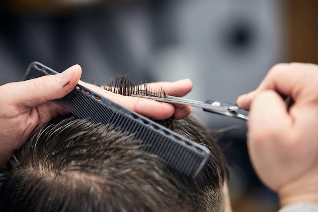 Profesjonalny fryzjer robi fryzurę młodemu mężczyźnie za pomocą nożyczek i grzebienia w salonie fryzjerskim