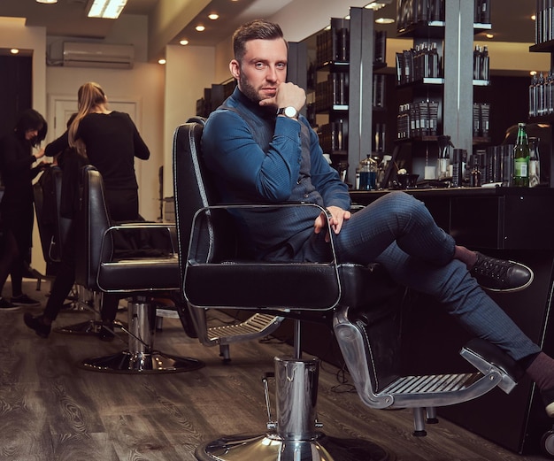 Profesjonalny fryzjer siedzący na fotelu fryzjerskim w oczekiwaniu na kolejnego klienta.