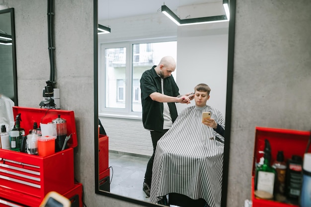 profesjonalny fryzjer tworzy modną fryzurę dla klienta z telefonem w dłoni