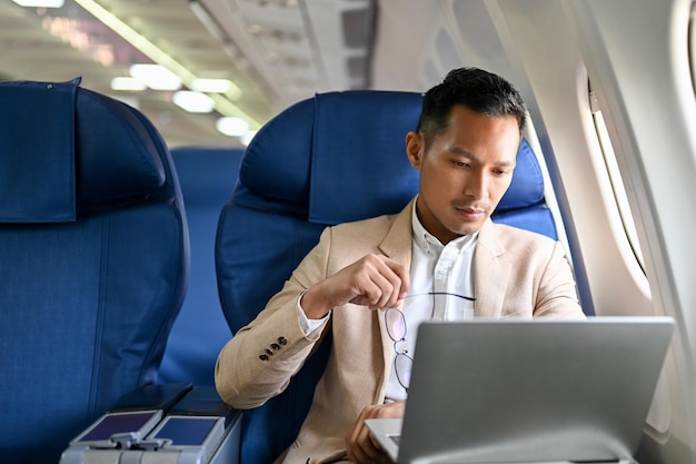 Profesjonalny i skoncentrowany azjatycki biznesmen korzystający z laptopa podczas lotu