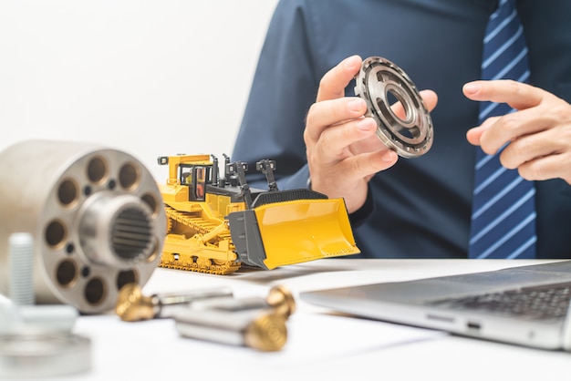 Zdjęcie profesjonalny inżynier mechanik sprawdza płytkę zaworową hydraulicznej pompy tłokowej i pisze raporty z dnia roboczego w biurze, naprawy konserwacji ciężkich maszyn