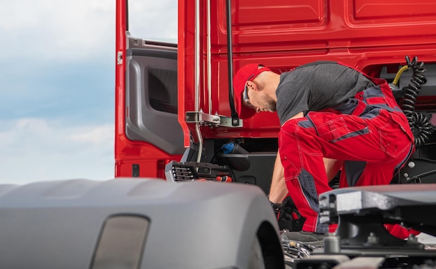 Zdjęcie profesjonalny kaukaski mechanik ciężarówek po czterdziestce, noszący czerwony mundur, wykonujący nowoczesne naprawy półciężarówek w przemyśle transportowym