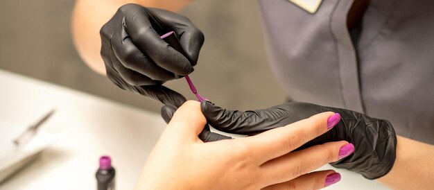 Profesjonalny manicure Manikiurzystka maluje kobiece paznokcie klientki fioletowym lakierem do paznokci w salonie kosmetycznym z bliska Koncepcja branży kosmetycznej