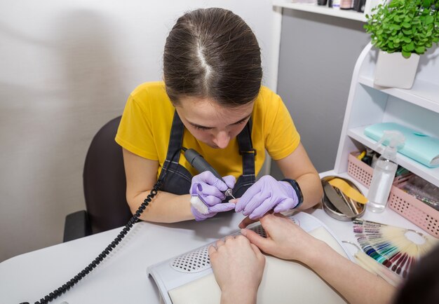 Profesjonalny manicure sprzętowy na maszynie elektrycznej w salonie kosmetycznym. Mistrz używa elektrycznej maszyny do usuwania lakieru z rąk podczas manicure.