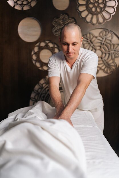 Profesjonalny masażysta wykonujący masaż antycellulitowy na nogach blondynki zrelaksowanej kobiety leżącej na stole w salonie spa