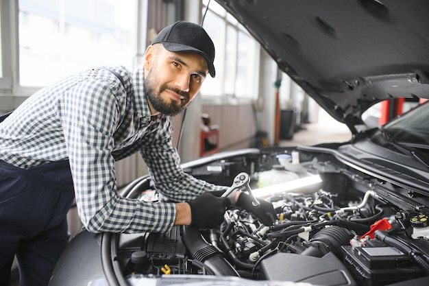 Profesjonalny mechanik pracuje przy samochodzie w warsztacie samochodowym Mechanik w okularach ochronnych naprawia silnik w pojeździe Specjalista odkręca śruby za pomocą grzechotki Nowoczesny warsztat czyszczenia