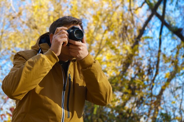 Profesjonalny męski fotograf fotografujący na świeżym powietrzu w jesiennym żółtym lesie na nowoczesnym aparacie dslr