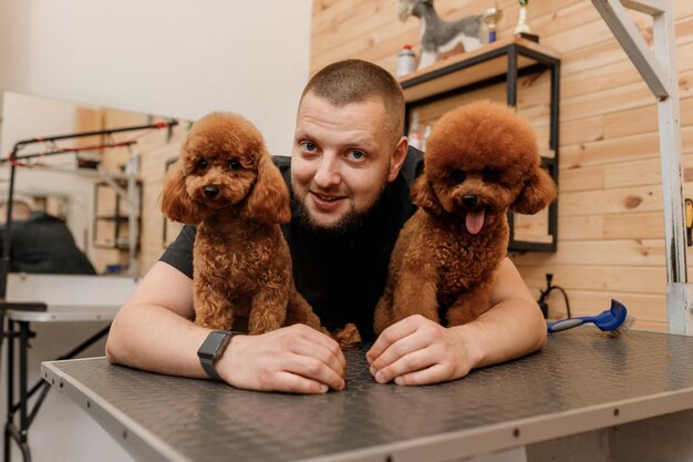 Profesjonalny Męski Groomer Z Psem Z Filiżanką Pudla W Swoim Miejscu Pracy W Salonie Pielęgnacyjnym Dla Zwierząt Domowych