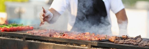 Profesjonalny męski szef kuchni smażący świeże mięso na grillu na świeżym powietrzu