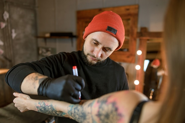 Profesjonalny mężczyzna, brodaty kaukaski mistrz tatuażu pracuje w przytulnym, klimatycznym studio