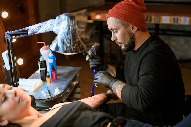 Zdjęcie profesjonalny mężczyzna, brodaty kaukaski mistrz tatuażu pracuje w przytulnym, klimatycznym studio