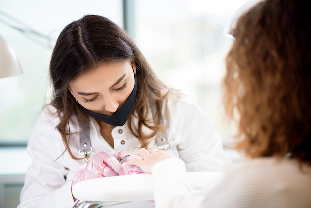 Profesjonalny mistrz manicure w ochronnej masce na twarz za pomocą elektrycznego narzędzia do polerowania paznokci do zabiegu manicure z glazurą