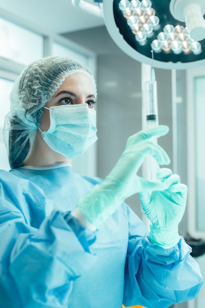 Profesjonalny pracownik medyczny stojący na sali operacyjnej ze strzykawką w dłoni i patrzący na nią