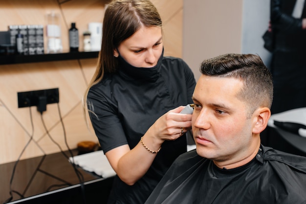 Profesjonalny stylista w nowoczesnym, stylowym zakładzie fryzjerskim goli i obcina włosy młodego mężczyzny. Salon kosmetyczny, salon fryzjerski.